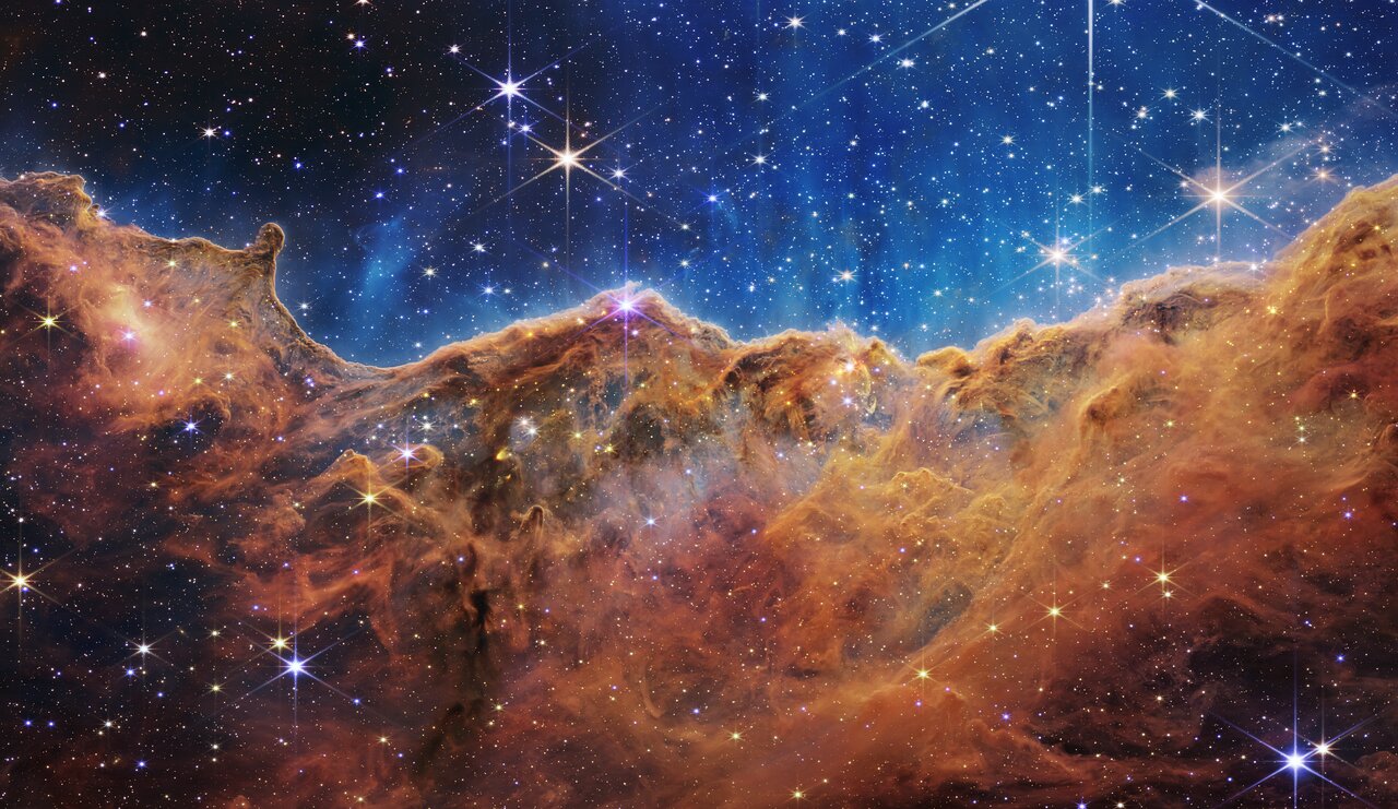 The Cosmic Cliffs: a wall of orange gas and dust below a blue cavity scattered with stars