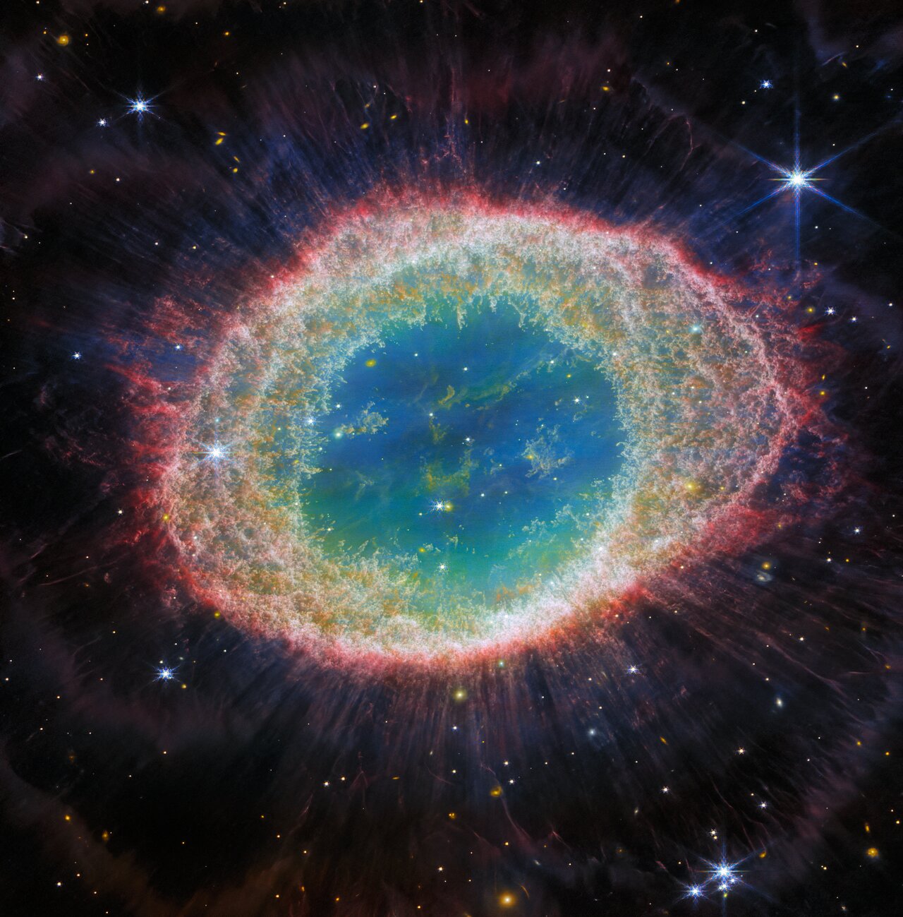 The Ring Nebula in infrared: an oval ring of orange and red filaments around a pale blue-green interior with a tiny central star